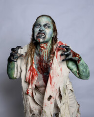 Close up portrait of scary female model wearing spooky halloween costume, ripped apocalyptic clothes, dropping fake blood like an undead zombie character. Isolated figure on studio background