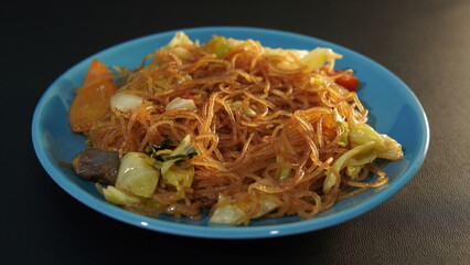 Fried vermicelli ( bihun goreng ) on a blue plate on a black background