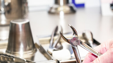 A dentist holds dental pliers in a sterile environment.Several other medical instruments are visible in the background.