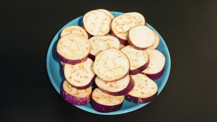 sliced ​​purple eggplant on a blue plate on a black background