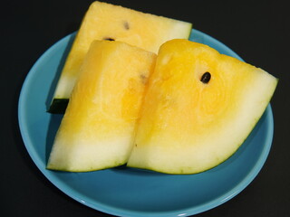 yellow watermelon slices on a blue plate on a black background