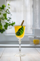 Yellow cocktail standing on white table with leaf garnish