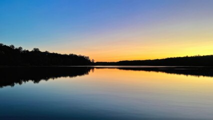 Obraz premium A serene sunset over a calm lake, reflecting vibrant colors and surrounding trees.