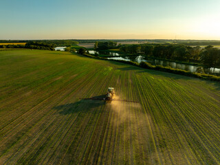 Drone shot of a tractor spraying in lush green wheat fields under the bright sun, showcasing modern agriculture