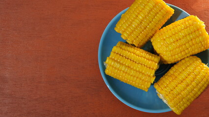several pieces of boiled corn on a blue plate on the table. flat lay. theme of healthy eating and diet. boiled corn (jagung rebus)	
