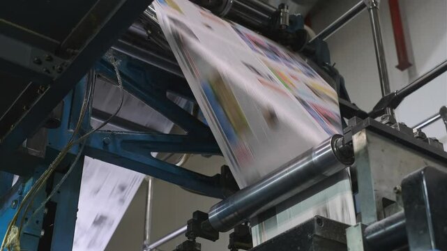 High-speed printing press in action as it efficiently prints colorful newspapers in a modern industrial printing house.