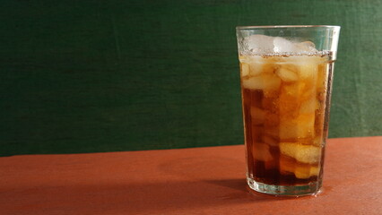 A glass of iced tea on a wooden table with a green wooden plank in the background