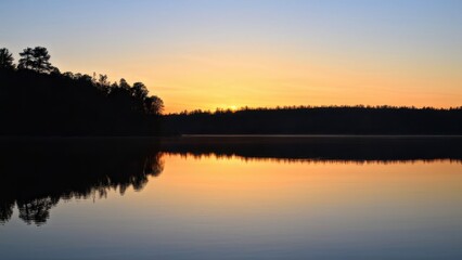 Obraz premium A serene lake at sunset, reflecting vibrant colors and silhouettes of trees.