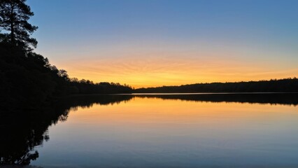 Obraz premium A serene lake at sunset, reflecting vibrant colors in the sky.