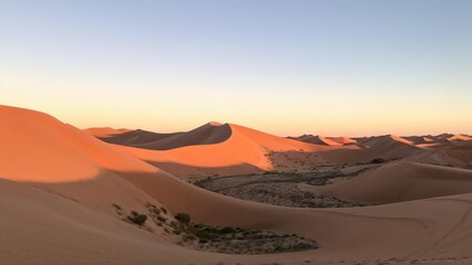 A serene desert landscape at sunset, showcasing rolling sand dunes and a clear sky.