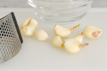 Garlic cloves and garlic press close-up on a white cutting board