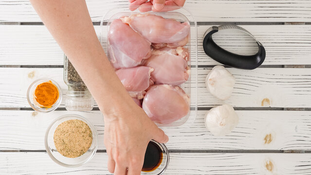 Chef marinating chicken thighs with soy sauce, turmeric, black pepper, seasoning, and fresh garlic. The cooking process, ingredients close-up
