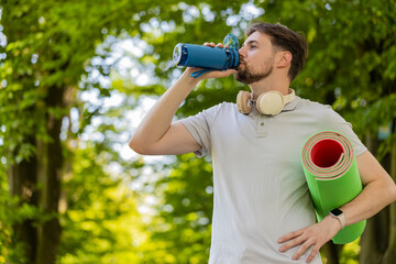 Athletic fitness sport runner with yoga mat drinking water from bottle after training exercise....