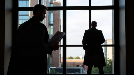 Two men reading and standing by window in office
