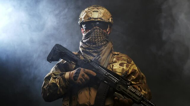 A courageous soldier in a protective combat uniform with a machine gun standing on a dark background, shrouded in smoke. War and military concept.