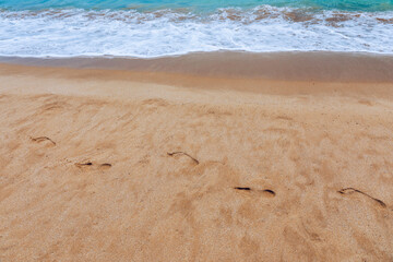 Footsteps in the sand. Footprints in the sand beach. Footprints in the sand against a sea wave. Footprints on a sunny day with golden sand, beach, wave and footsteps.