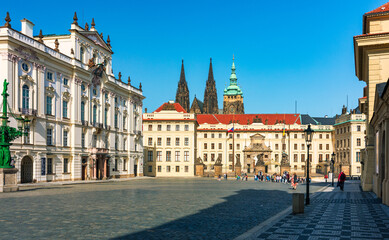 Fototapeta premium Cobblestone street winding through historic buildings in Prague with St. Vitus Cathedral. Street leads past historical buildings in Prague, showcasing the iconic spires of St. Vitus Cathedral, Prague.