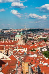 Naklejka premium Panoramic view of Prague featuring historic buildings and vibrant rooftops on a sunny day in summer. View of Prague, Czech Republic, showcasing the city's iconic architecture and red-tiled roofs.