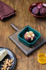 Fototapeta premium Fresh figs stuffed with blue cheese and walnuts in a portioned ceramic dish before baking on a wooden background. Fig recipes.