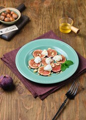 Dessert, fresh fig carpaccio with ricotta, hazelnuts and honey on a green plate on a wooden background. Fig recipes. Healthy desserts.