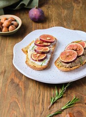 Two open sandwiches with fresh figs, ricotta and pate on a light ceramic plate on a wooden background. Recipes figs.