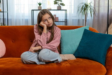Portrait of calm brunette little girl sitting alone on couch in living room at home. Preteen...
