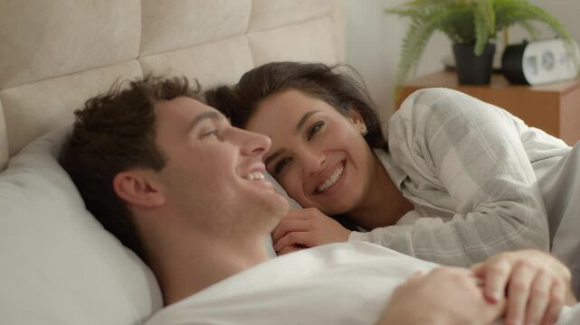 Two people happy couple man woman lying together bed bedroom home communicate talking chatting smiling laughing male female mutual understanding conversation sweetheart honeymoon bond moment feeling