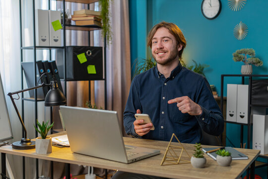 Smiling businessman using smartphone app online pointing showing remote distance job working from home office. Man freelancer guy e-learning texting messages content on social media.