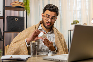 Health, cold, and people concepts. Sick young Arabian businessman wrapped in blanket works on...