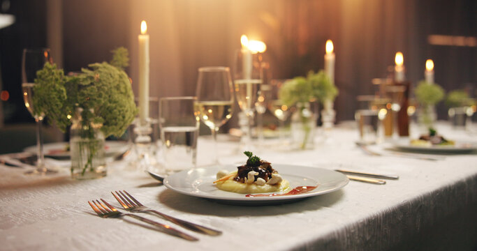 Plate, food and empty dinner table at event with catering, candles and service for gala at night. Meal, party and glass for water, alcohol or drinks with luxury, interior or furniture for fine dining