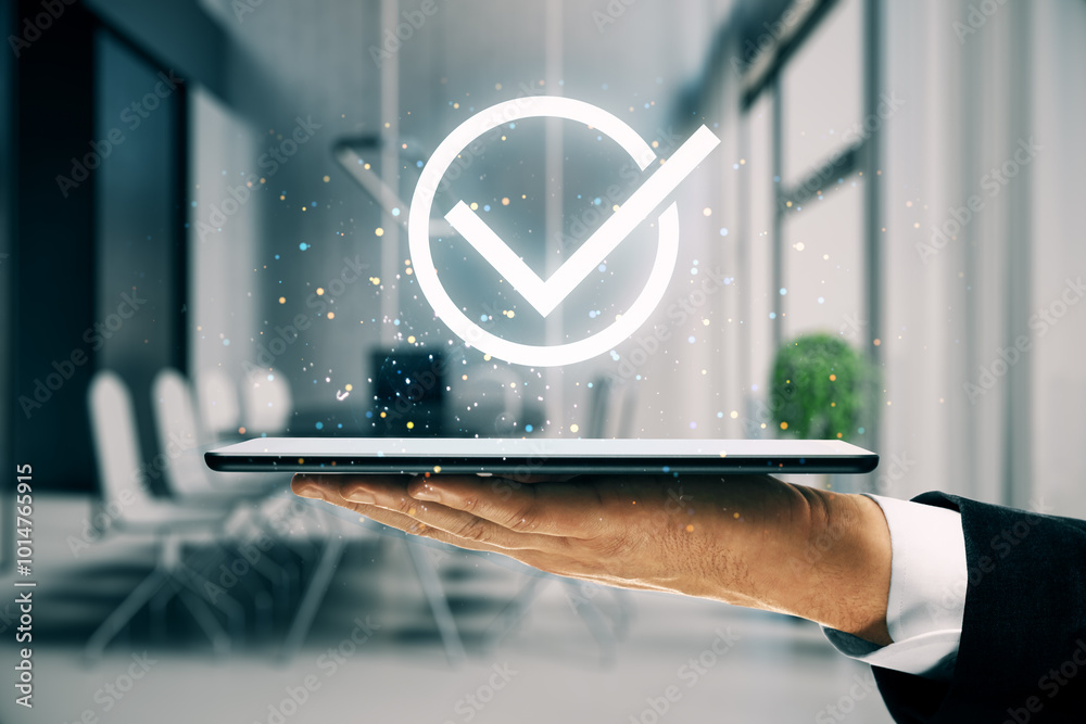 Poster hand holding tablet with glowing check mark icon in modern office setting.