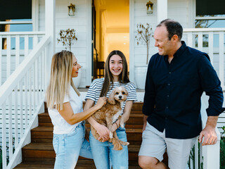 Young teenage girl carrying a dog while standing beside her parents outside the house.