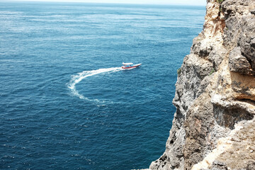 Speed boat with wave crashing rocky cliff at the blue sea and destination travel summer ocean in Bali island at Indonesia