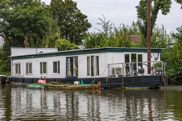 Houseboat with white walls and flat roof anchored on bank of shipping canal outside the city of...