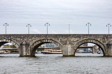 Sint Servaasbrug bridge over river Meuse, street post lamps, boats and parts of buildings in background, calm water, cityscape of city of Maastricht in South Limburg, Netherlands