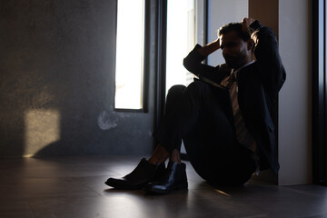 A male professional sits on the floor, visibly affected by the disappointment stemming from the...