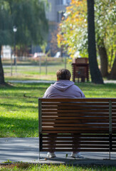 A man sits on a park bench, looking at the ground