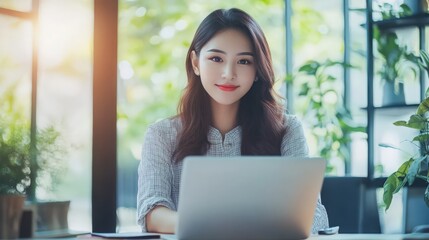 Portrait of a cheerful Asian businesswoman using a laptop and writing on a charger to keep notes as a base Analyze, and gather thoughts and ideas happily in her office.