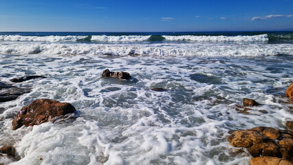 Balearic Sea, Salou, Spain. Beach, turquoise transparent sea, small waves. Landscape on the coast, rocks. Vacation at sea