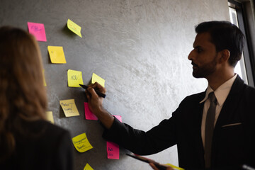 A businessman is shown in a meeting room, holding a pen and writing on blank paper. The image...