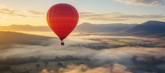 Obraz premium A red hot air balloon is flying over a misty valley in the Australian countryside at sunrise
