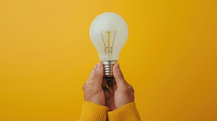 hands holding a light bulb against a vibrant yellow background, symbolizing creativity, innovation, new ideas, and energy.