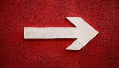 A white arrow painted on a stucco wall, pointing towards the right in an outdoor setting. Red wall