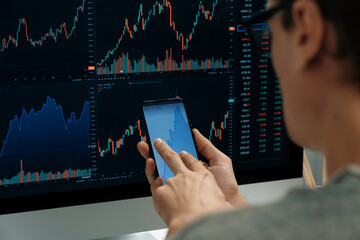 Smart stock investors pointing on screen with smartphone for market stock exchange along with laptop screen in highest dynamic investment rate, focusing data planning at modern workplace. Pecuniary.