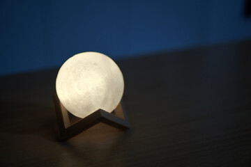 Hands holding an illuminated moon-like sphere lamp against a dark backdrop