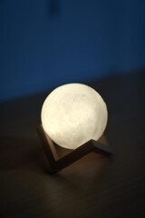 Hands holding an illuminated moon-like sphere lamp against a dark backdrop