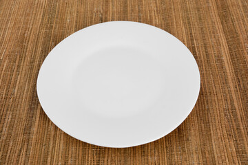 A white plate sits on a brown tablecloth.