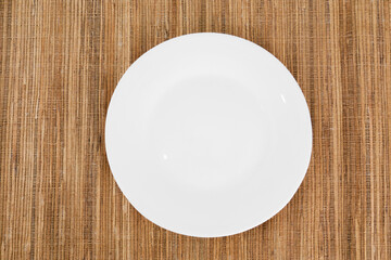 A white plate sits on a brown tablecloth.
