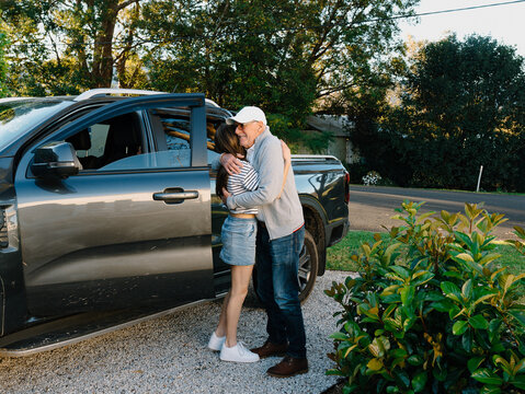Grandfather embracing granddaughter outside by the car