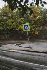 Pedestrian crossing sign on a wet road at a roundabout